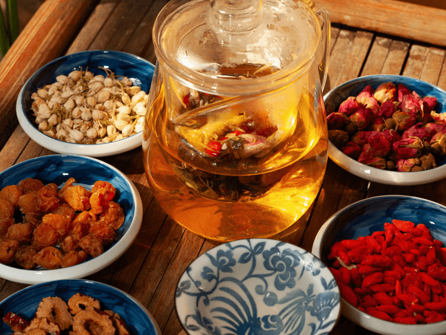 Bàn gỗ với các nguyên liệu làm nước detox như trái cây khô, thảo mộc và bình trà thủy tinh